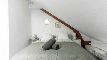 A bedroom with a sloped ceiling, a bed with a quilted green bedspread, a wooden headboard, and a bedside table with a lamp.
