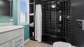 Um banheiro com chuveiro em azulejos pretos, vaso sanitário branco e pia com bancada de mármore.