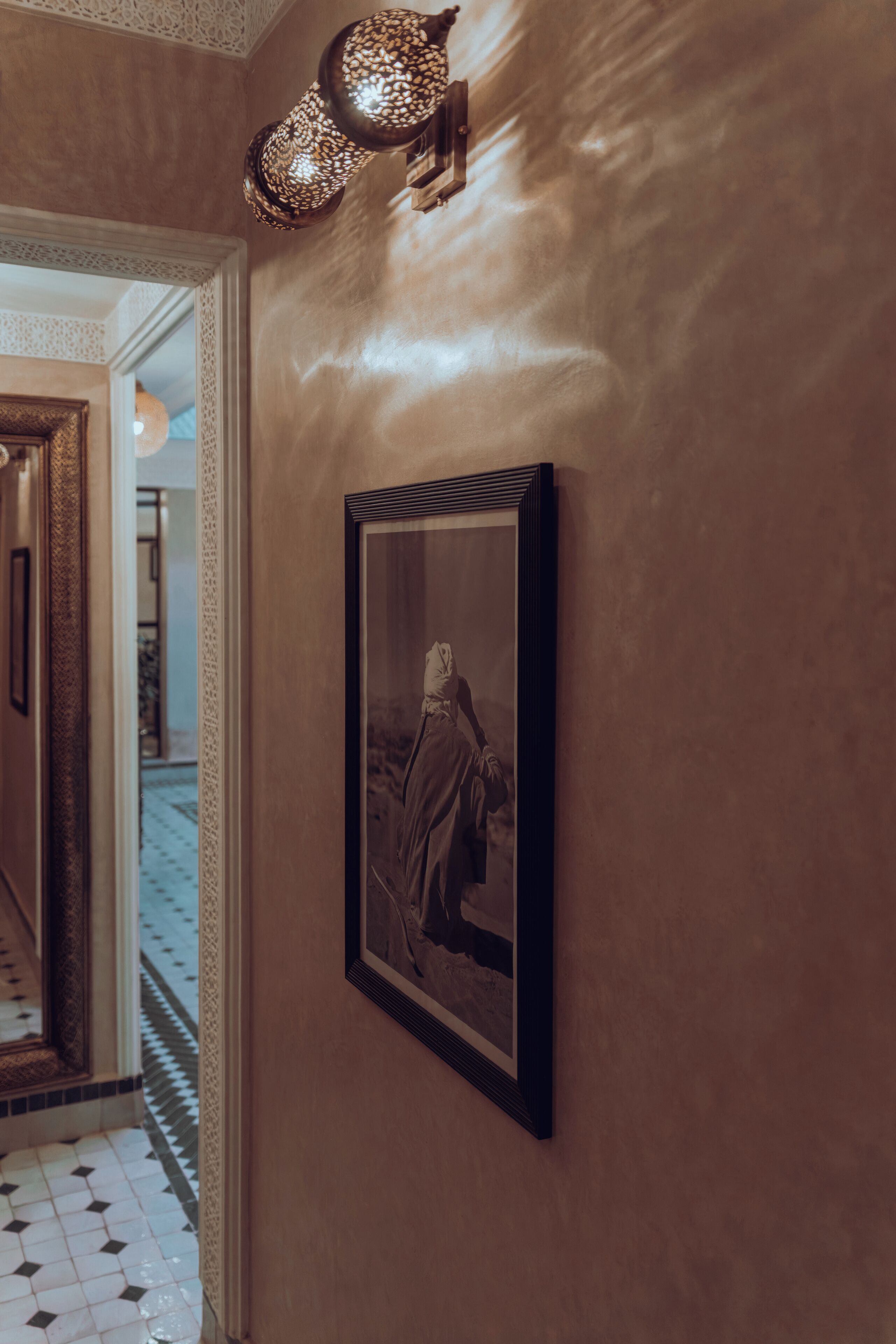 A hallway with a framed picture on the wall, a patterned floor, and a decorative light fixture.