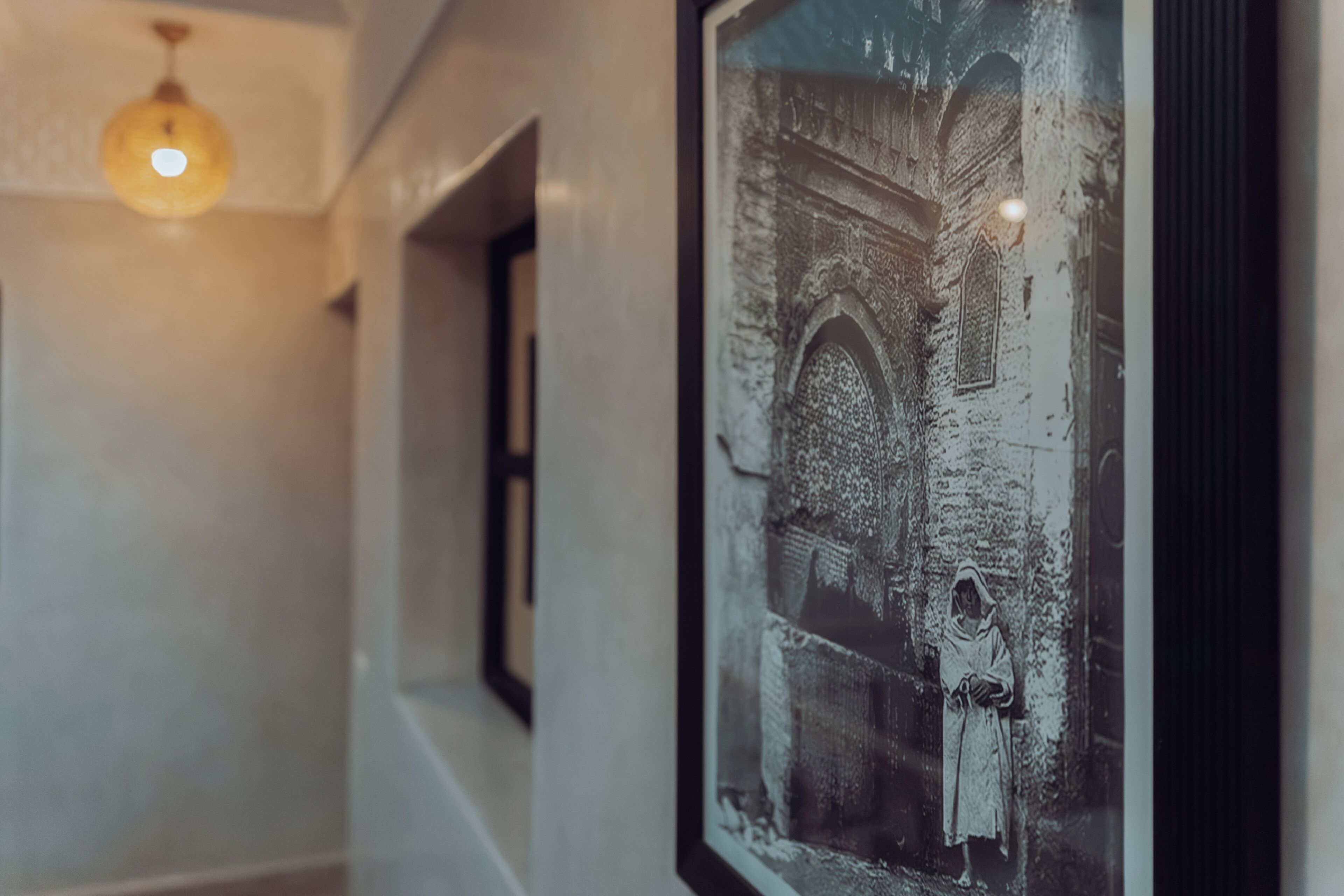Un couloir orné d’une photographie historique encadrée au mur, d’un luminaire suspendu et d’une fenêtre donnant sur un bâtiment.