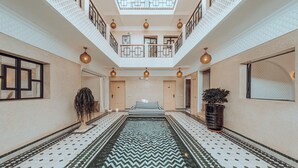 A spacious atrium with a patterned floor, a central water feature, and a balcony with railings and hanging lights.