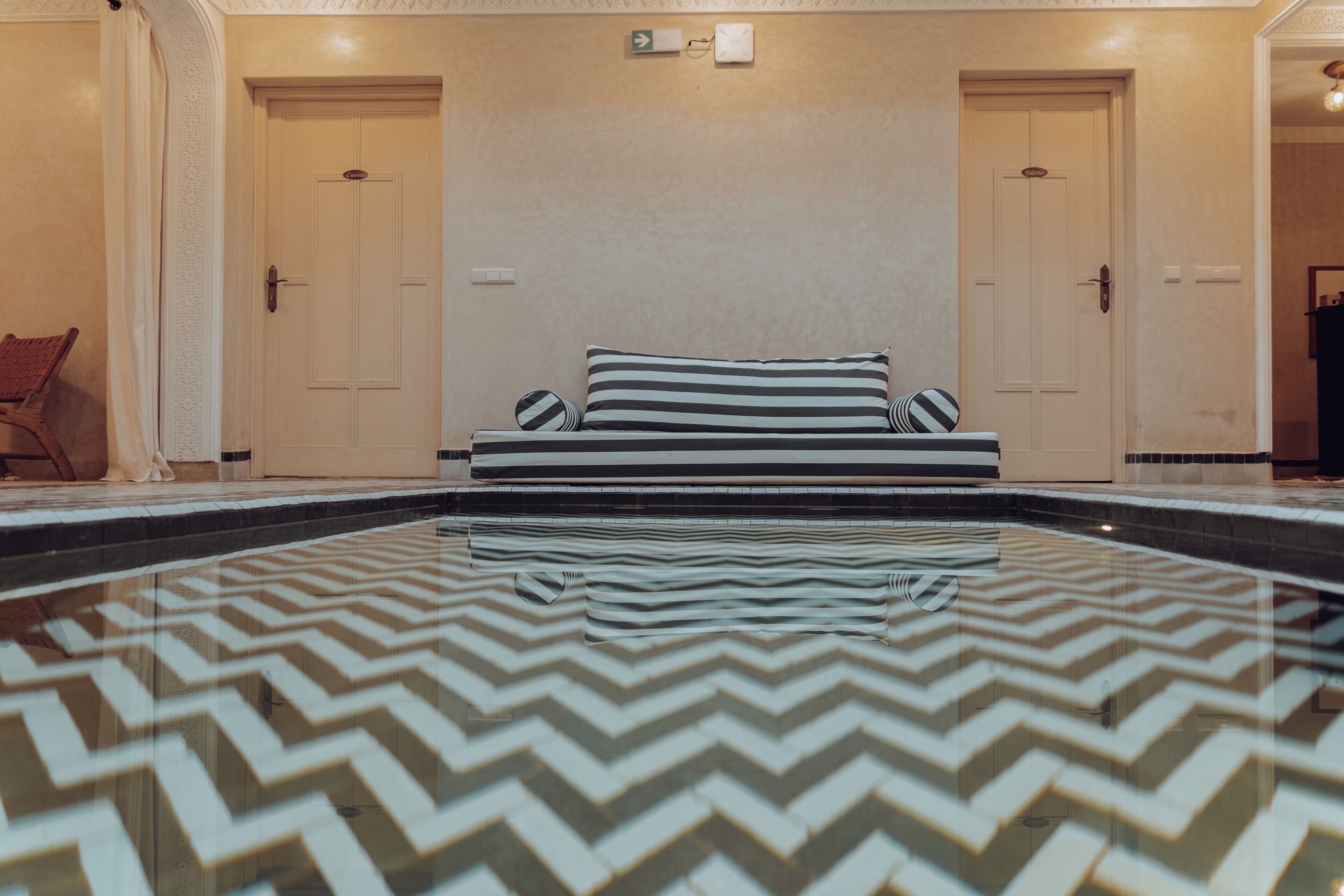 A hotel room with a large, patterned swimming pool, a bed with striped pillows, and two doors.
