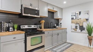 A modern kitchen with grey cabinets, a black stove, a microwave, and a tiled backsplash. - Family-Friendly 2BR Getaway (Austell)
