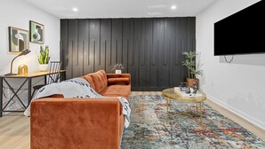 A modern living room with a brown sofa, a small round table, and a dark wooden accent wall. - Family-Friendly 2BR Getaway (Austell)