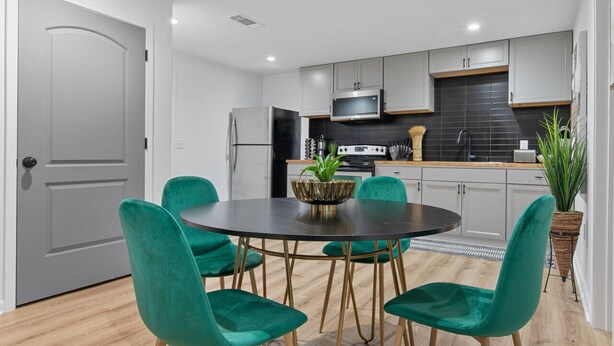 A modern kitchen with grey cabinets, a black countertop, and a round table with teal chairs. - Family-Friendly 2BR Getaway (Austell)