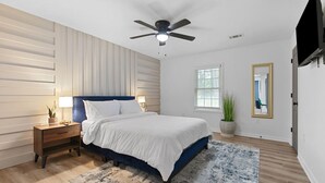 A bedroom with a bed, nightstand, ceiling fan, window, and a mirror on the wall. - Family-Friendly 2BR Getaway (Austell)