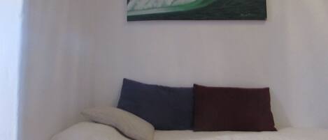 A bed with a white quilted bedspread, two pillows (one dark blue, one maroon), and a painting of a wave on the wall.