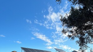 Een wit gebouw met een zwarte deur, zonnepanelen op het dak en een houten hek ervoor.
