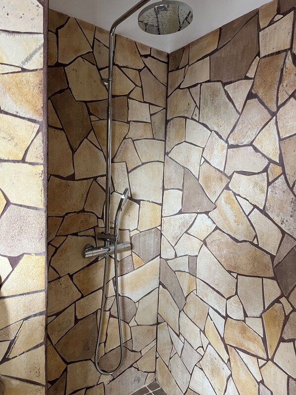 A shower with a stone wall design and a round mirror above the sink.
