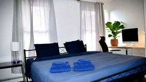 A hotel room with a bed, a desk, a chair, a potted plant, and a television.