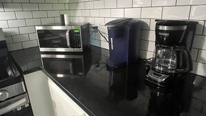 Una cocina con armarios blancos, encimera negra, microondas, cafetera y tostadora.