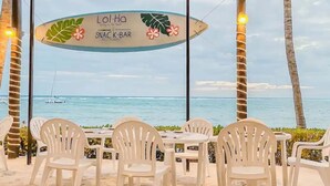 Un bar de aperitivos frente a la playa, con sillas de plástico blanco y vista al océano.