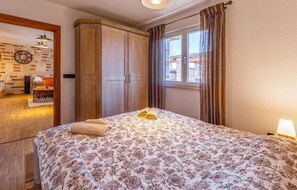 A bedroom with a bed, a wooden wardrobe, a window with curtains, and a wall clock. - Villa Azimut - Cozy Home In Medulin With Sauna (Medulin)