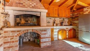 A rustic kitchen with a stone fireplace, wooden cabinets, and a modern refrigerator. - Villa Azimut - Cozy Home In Medulin With Sauna (Medulin)