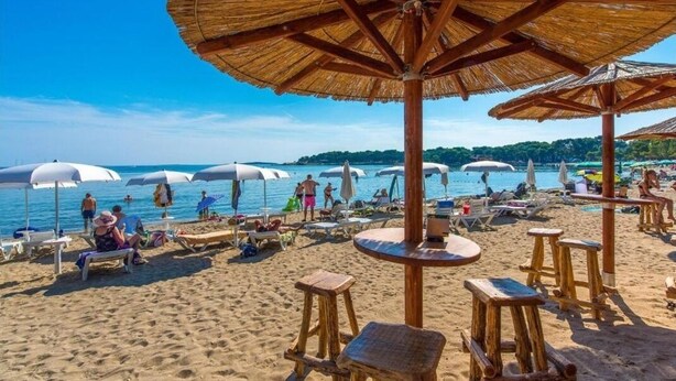 A beach with thatched umbrellas and wooden tables, providing shade and seating for visitors. - Villa Azimut - Cozy Home In Medulin With Sauna (Medulin)