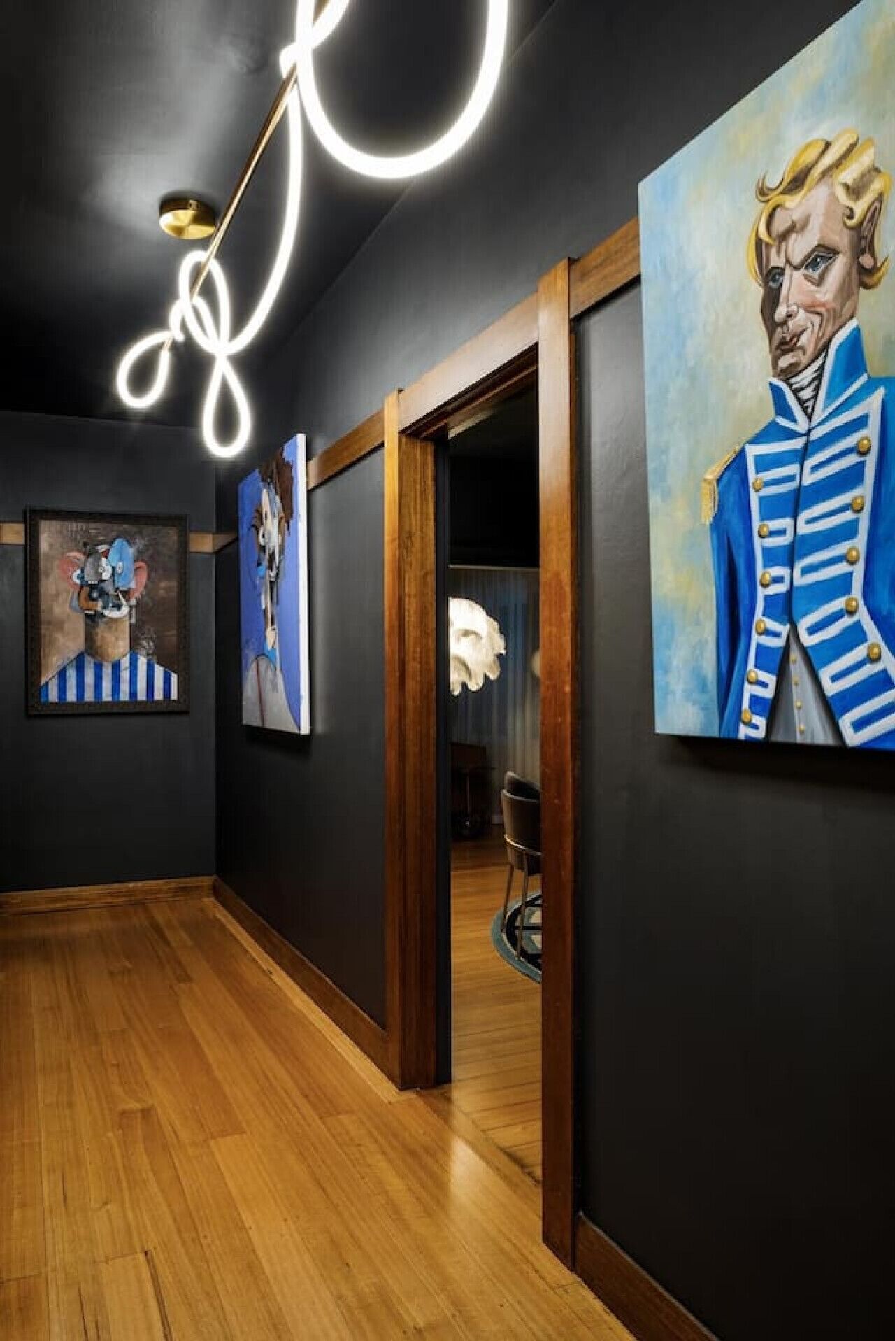 Un pasillo con suelo de madera, una luz de neón y varias pinturas en las paredes.