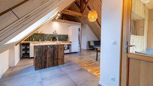 Et moderne køkken med en træø i midten, et spiseområde med bænk og et soveværelse i et hvælvet loft.