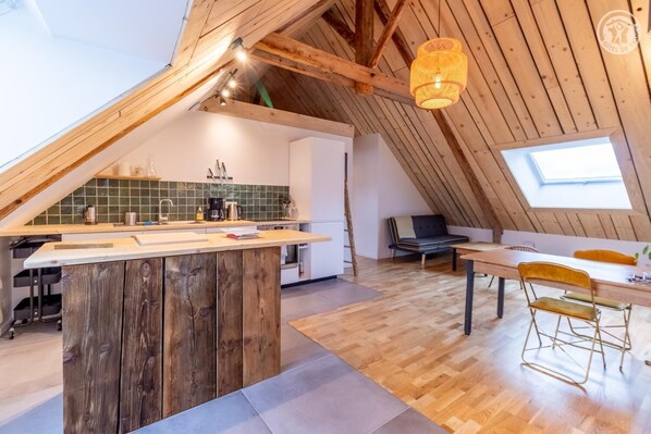Enjoy a spacious loft-style living area with a central kitchenette, dining table, and natural light pouring in through the skylight.