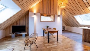 Et rum med højt til loftet, trævægge, et spisebord, stole, et fjernsyn og en hængende lampe.