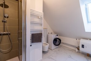 Bathroom features a shower area, toilet, and front-loading washing machine.