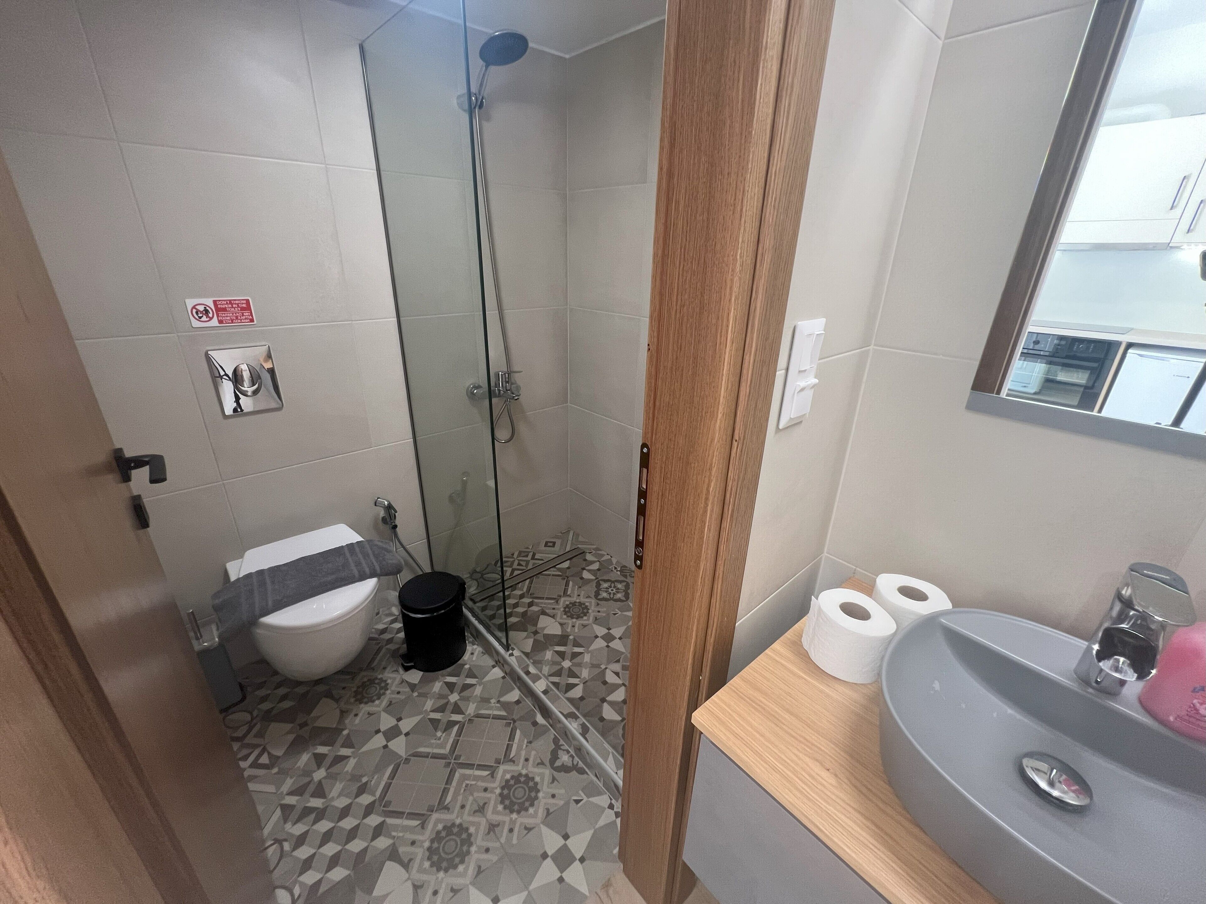 Een badkamer met douche, toilet, wastafel en vloertegels met een patroon.