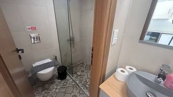 Een badkamer met douche, toilet, wastafel en vloertegels met een patroon.