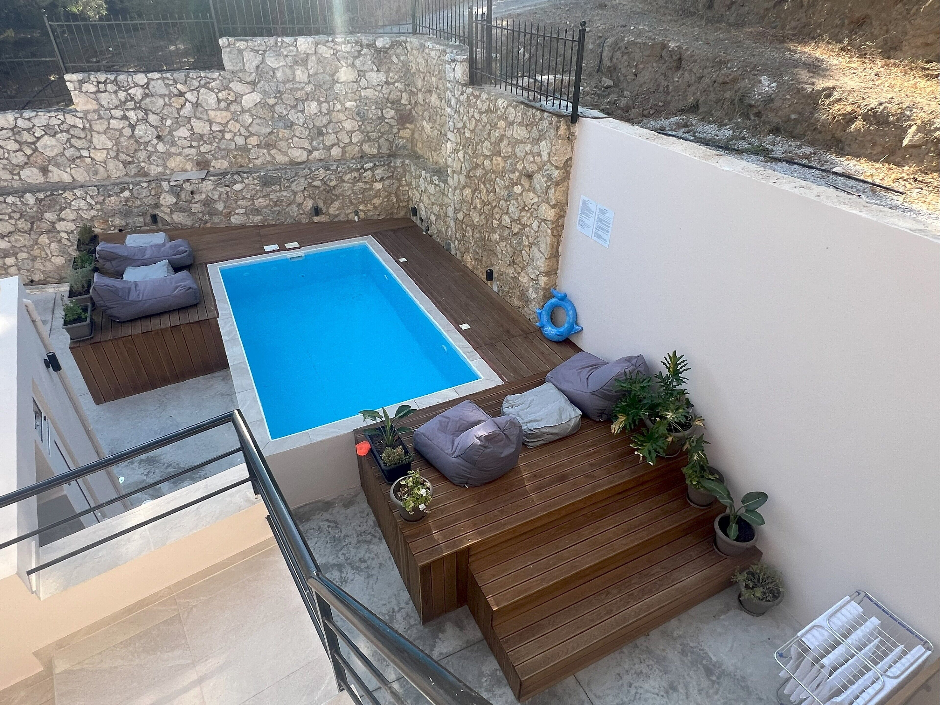 A rooftop pool area with stone walls, wooden deck, and seating.