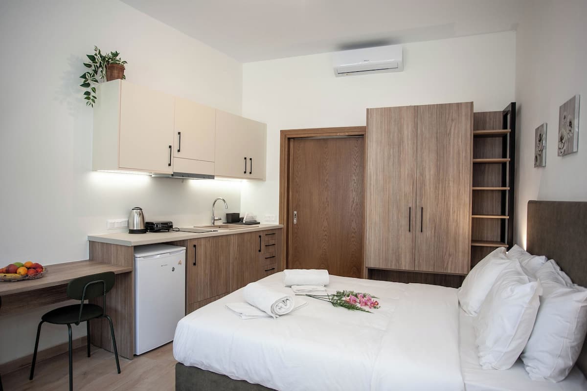 A modern hotel room with a bed, a desk with a kettle, a small refrigerator, and a wooden wardrobe.