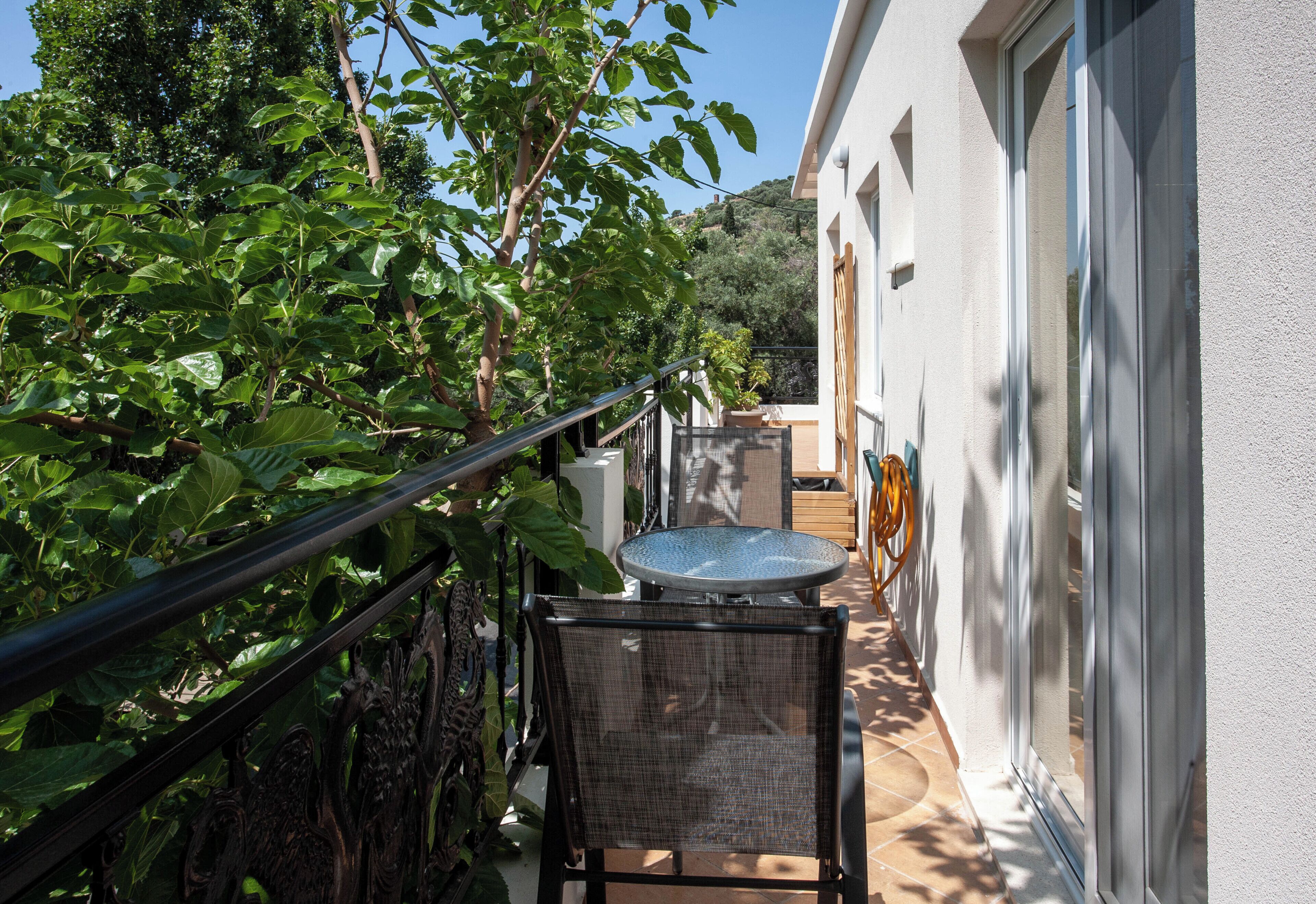 Un étroit couloir extérieur, doté d’une rambarde en métal, d’une table ronde et d’une chaise, qui mène à l’entrée d’un bâtiment.