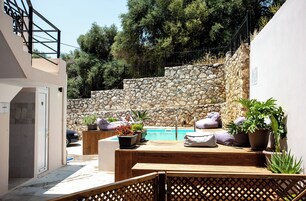 Un área junto a la piscina con paredes de piedra, asientos de madera y plantas en macetas.