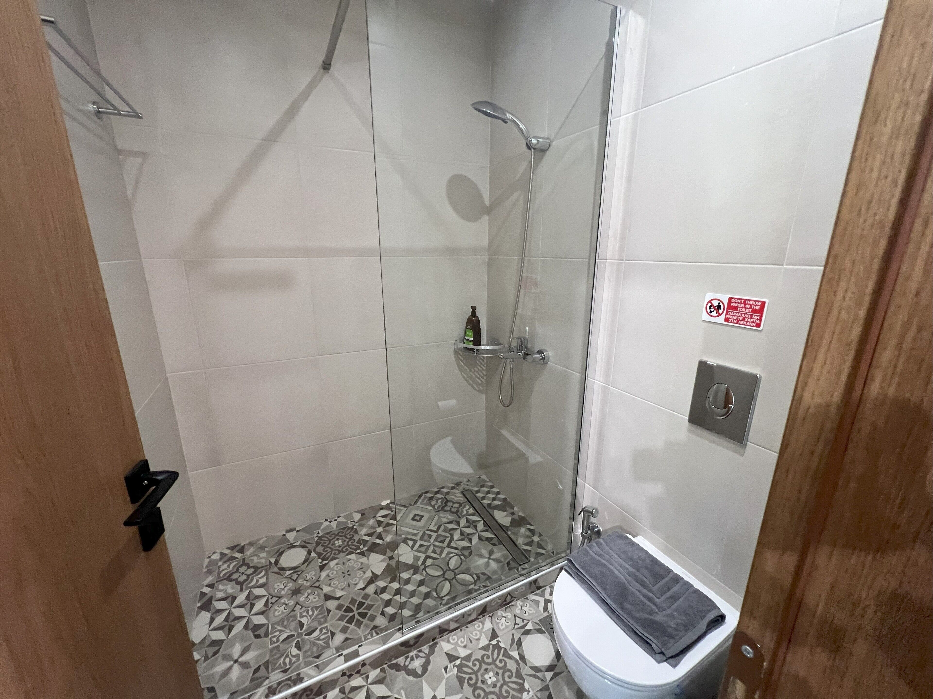 A shower with a glass door, a toilet with a towel, and a patterned floor.
