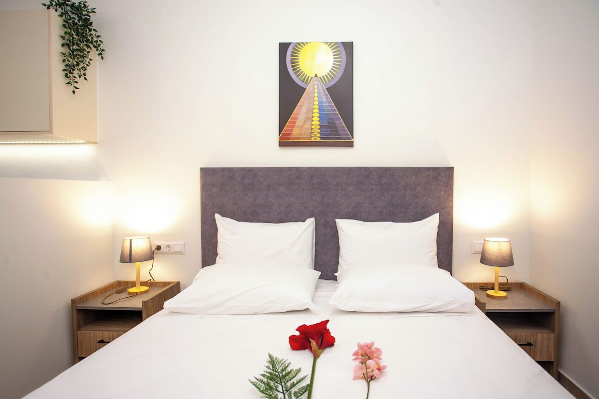A hotel room with a large bed, two bedside tables with lamps, a wall-mounted artwork, and a plant.