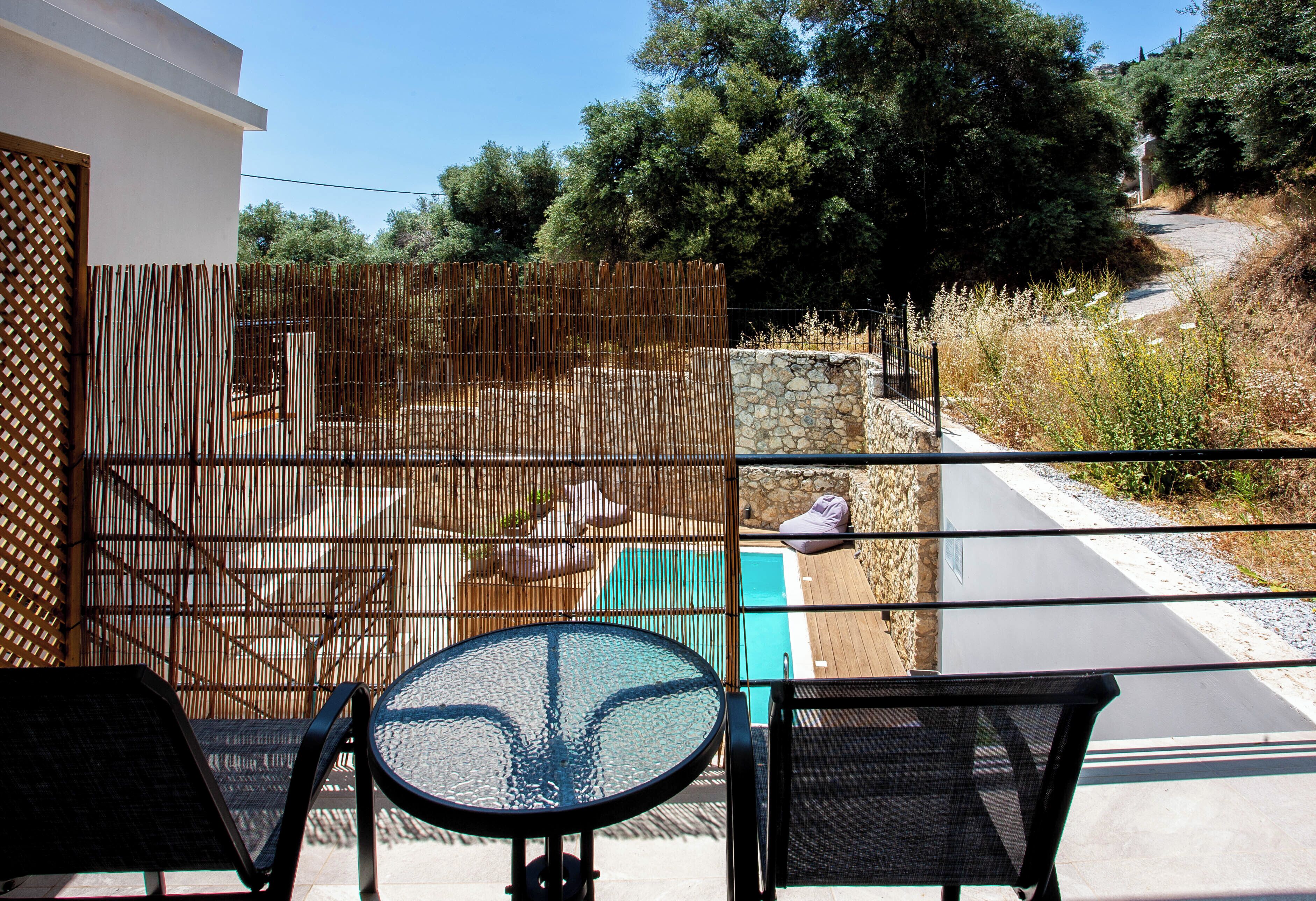 Un balcone con un tavolo e sedie in vetro, affacciato su una piscina e un muro in pietra.