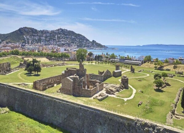 Une forteresse antique, avec des ruines, un mur d’enceinte et une vue sur une ville côtière et la mer.