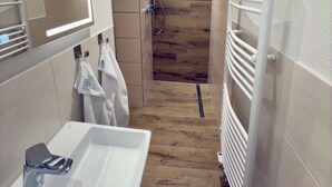 A modern bathroom with a wooden floor, a white sink with a chrome faucet, a mirror with a circular light, and a shower area with a wooden wall. - Historic living near the town hall and Steintor (Malchin)