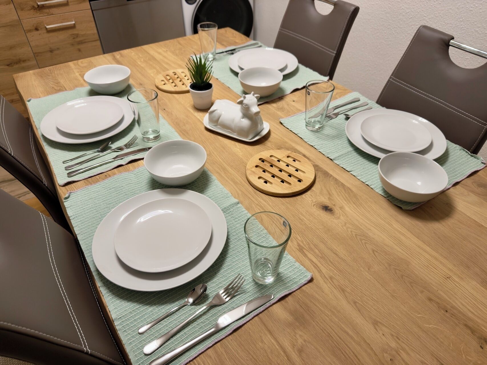 Een gedekte eettafel met borden, kommen, bestek en glazen, plus een kleine potplant en een decoratief paardje.