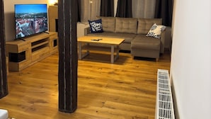 A living room with a wooden floor, a sofa, a coffee table, a TV, and a radiator. - Historic living near the town hall and Steintor (Malchin)