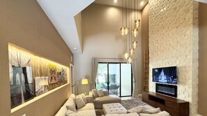 A modern living room with a sectional sofa, a flat-screen TV, and a brick-patterned wall. - Stay Near Disney Magic | Gorgeous 4BR Villa w BBQ (Kissimmee)