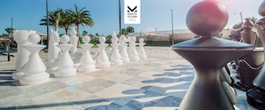 A chessboard with oversized chess pieces on a tiled surface, palm trees, and a clear sky.