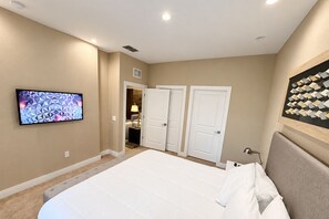 A bedroom with a large bed, a television mounted on the wall, and a door leading to another room. - Stay Near Disney Magic | Gorgeous 4BR Villa w BBQ (Kissimmee)