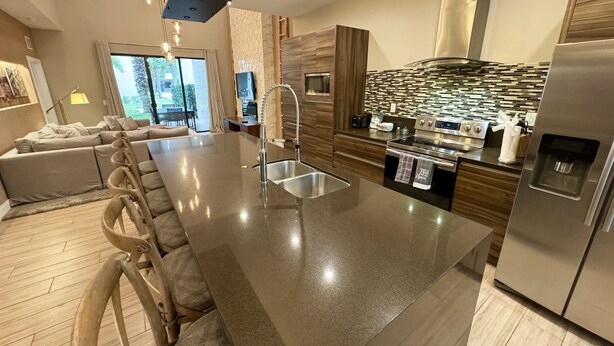 A modern kitchen with a central island, stainless steel appliances, and a large window. - Stay Near Disney Magic | Gorgeous 4BR Villa w BBQ (Kissimmee)