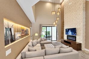 A modern living room with a sectional sofa, a flat-screen TV, and artwork on the walls. - Stay Near Disney Magic | Gorgeous 4BR Villa w BBQ (Kissimmee)
