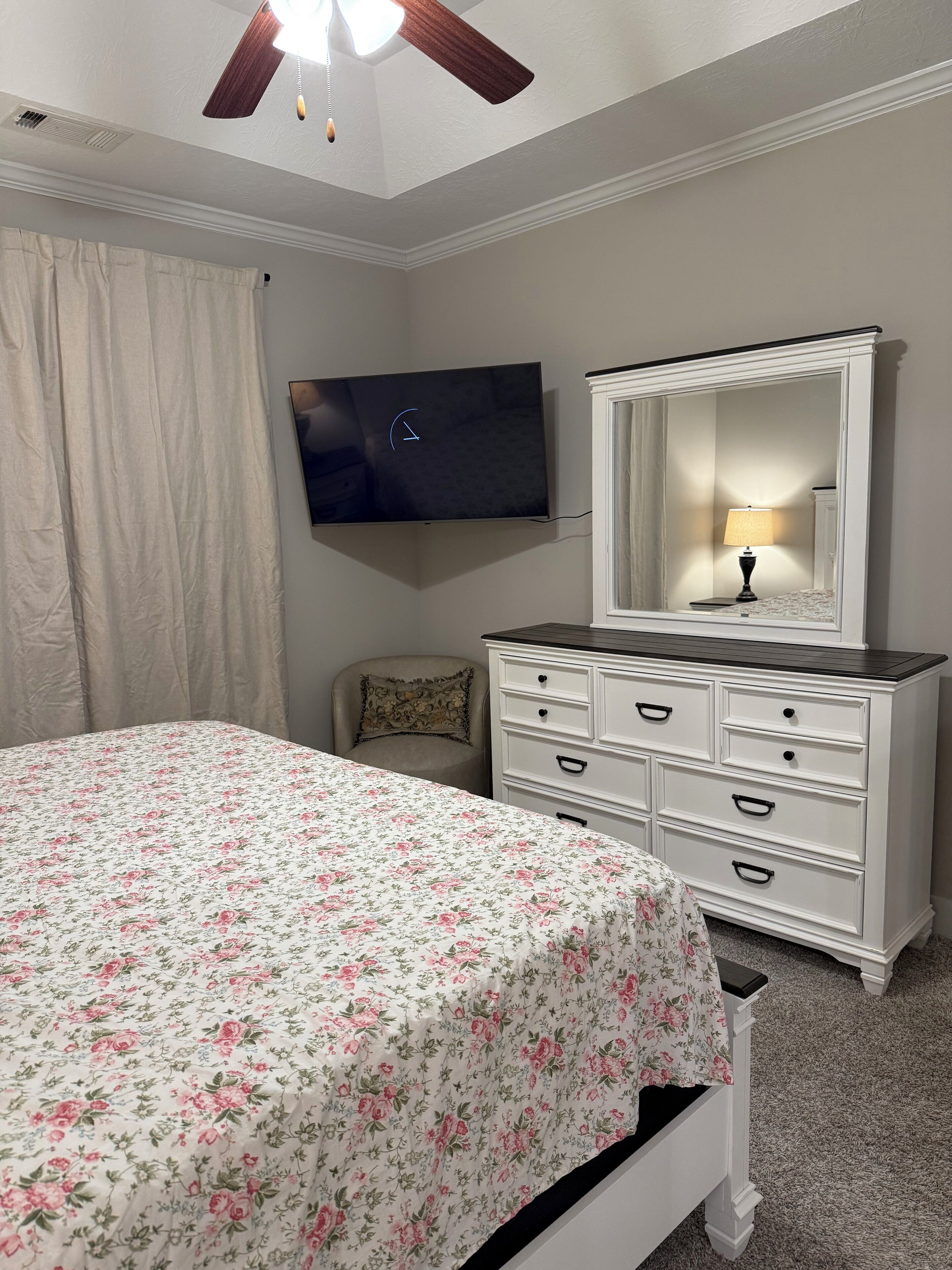 A bedroom with a bed, dresser, mirror, and ceiling fan.