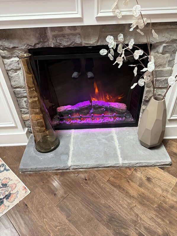 A fireplace with a stone surround, a decorative vase with white flowers, and a rug on the floor.