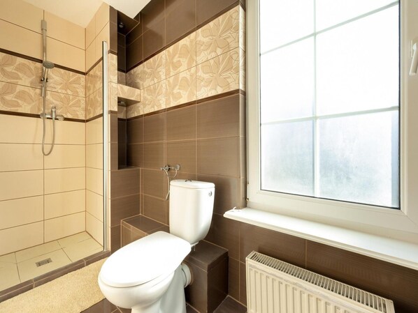 A modern bathroom with a shower, toilet, and a window providing natural light.