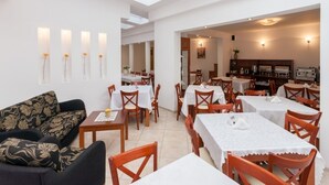 Zona pranzo con diversi tavoli e sedie, un divano e una cucina visibile attraverso un'apertura.