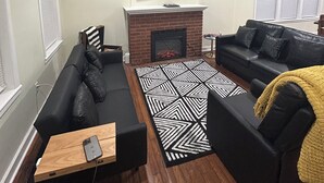 A living room with a fireplace, a ceiling fan, and a television mounted on the wall.