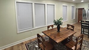 A dining area with a wooden table and chairs, a patterned rug, and a potted plant.