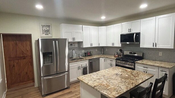 A modern kitchen with white cabinets, stainless steel appliances, and a granite countertop island with bar stools.
