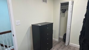 A room with a wooden floor, a black dresser, a closet with clothes, and a door.